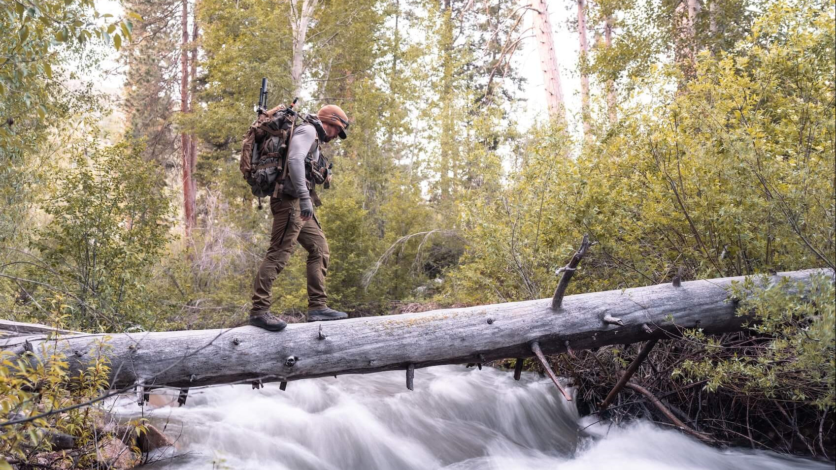 Hiker crossing a log over a stream in a forest